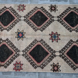 May include: A vintage rug with a cream background and a repeating pattern of black diamonds, brown and pink borders, and multi-colored stars.