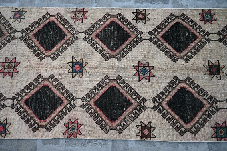 May include: A vintage rug with a cream background and a repeating pattern of black diamonds, brown and pink borders, and multi-colored stars.