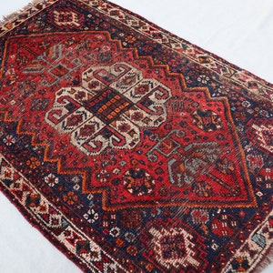 Pu&ograve; includere: Un tappeto vintage rosso, blu e bianco con un motivo geometrico. Il tappeto ha un bordo a frange ed &egrave; fatto di lana.