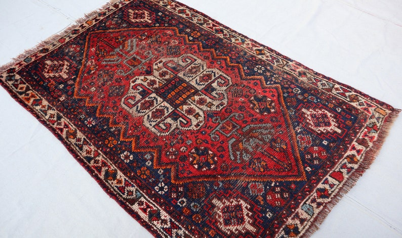 Pu&ograve; includere: Un tappeto vintage rosso, blu e bianco con un motivo geometrico. Il tappeto ha un bordo a frange ed &egrave; fatto di lana.