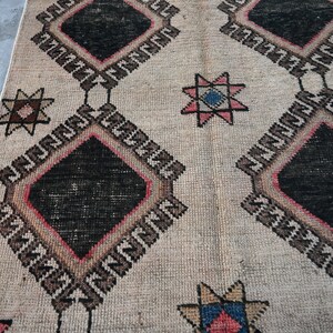 May include: A beige rug with a geometric pattern featuring black, red, and blue diamond shapes and star motifs. The rug has a distressed, vintage look.
