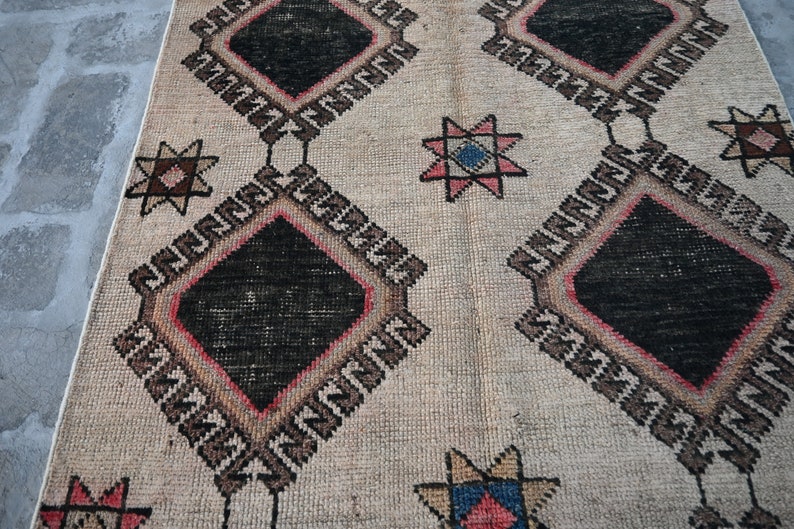 May include: A beige rug with a geometric pattern featuring black, red, and blue diamond shapes and star motifs. The rug has a distressed, vintage look.