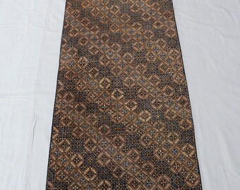 May include: A long, narrow rug with a geometric pattern in shades of brown, black, and orange. The rug has a fringe border.
