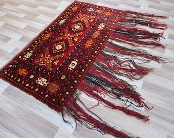 May include: A red, orange, and white patterned rug with a fringe border. The rug has a geometric design with a central diamond shape.