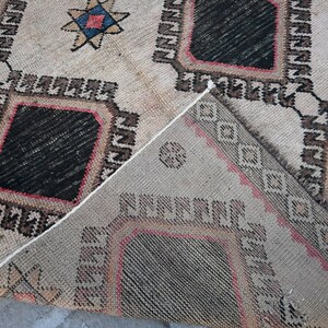 May include: A beige rug with a geometric pattern in black, red, and blue. The rug has a diamond shape in the center and is woven with a traditional design.