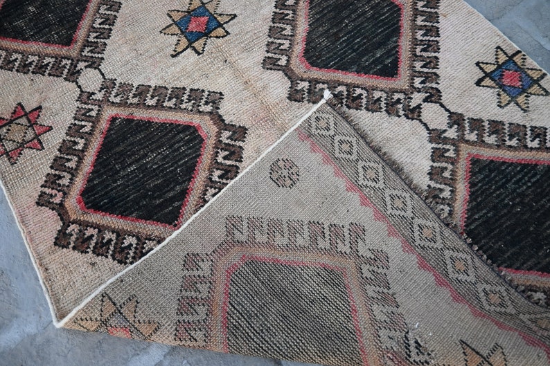 May include: A beige rug with a geometric pattern in black, red, and blue. The rug has a diamond shape in the center and is woven with a traditional design.