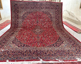 May include: A large rectangular area rug featuring a deep red central field with an intricate navy blue and cream floral medallion pattern. The rug is framed by a wide, detailed border in navy blue and red, finished with white fringe at the ends.