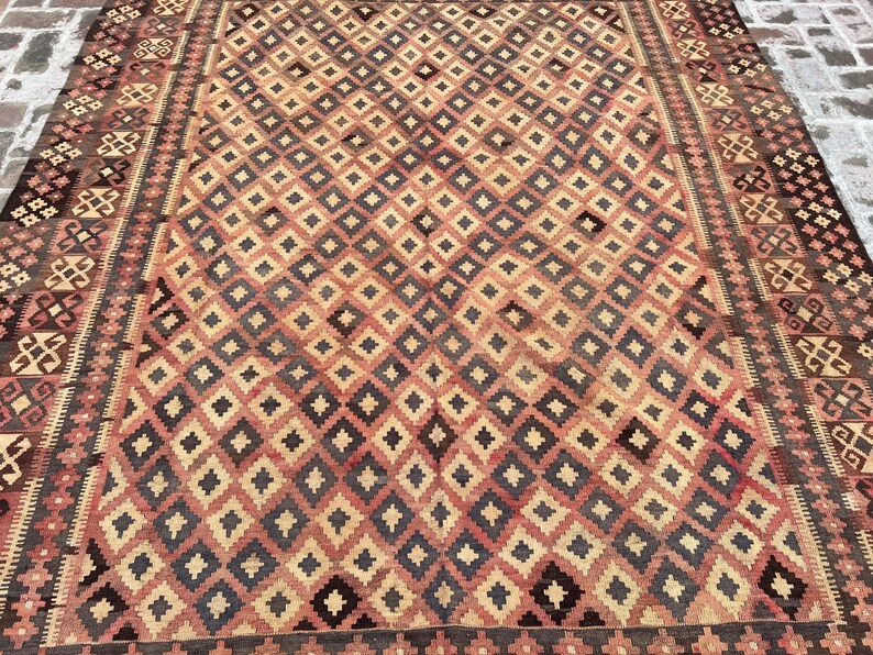 K&ouml;nnte beinhalten: Ein Vintage-Teppich mit einem geometrischen Muster in Rot-, Braun- und Cremet&ouml;nen. Der Teppich hat ein Rautenmuster mit einem Rand aus komplizierten Designs.