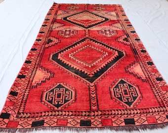 May include: A red, black, and cream colored rug with a geometric pattern. The rug has a diamond shape in the center and is surrounded by a border of smaller diamonds and other geometric shapes.