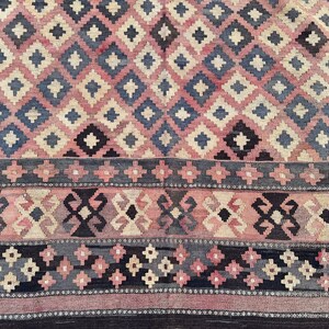 K&ouml;nnte beinhalten: Ein Vintage-Teppich mit einem geometrischen Muster in Rosa-, Blau- und Schwarzt&ouml;nen. Der Teppich hat ein Rautenmuster mit einem Rand aus kleineren geometrischen Formen.