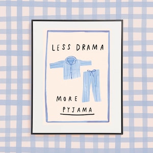 Pode incluir: Uma impressão emoldurada com o texto "Menos drama, mais pijama" em letras pretas. A impressão apresenta um top e calças de pijama listrados azul e branco.