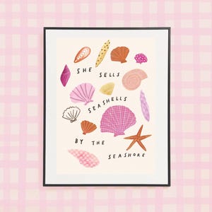 May include: A framed art print featuring a collection of colourful seashells and a starfish scattered across a cream background. The text "SHE SELLS SEASHELLS BY THE SEASHORE" is printed in black lettering among the various pink, orange, and yellow shells.