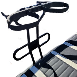 May include: Black metal golf cart cup holder with two straps for holding beverages. The cup holder is mounted on the back of a golf cart seat.