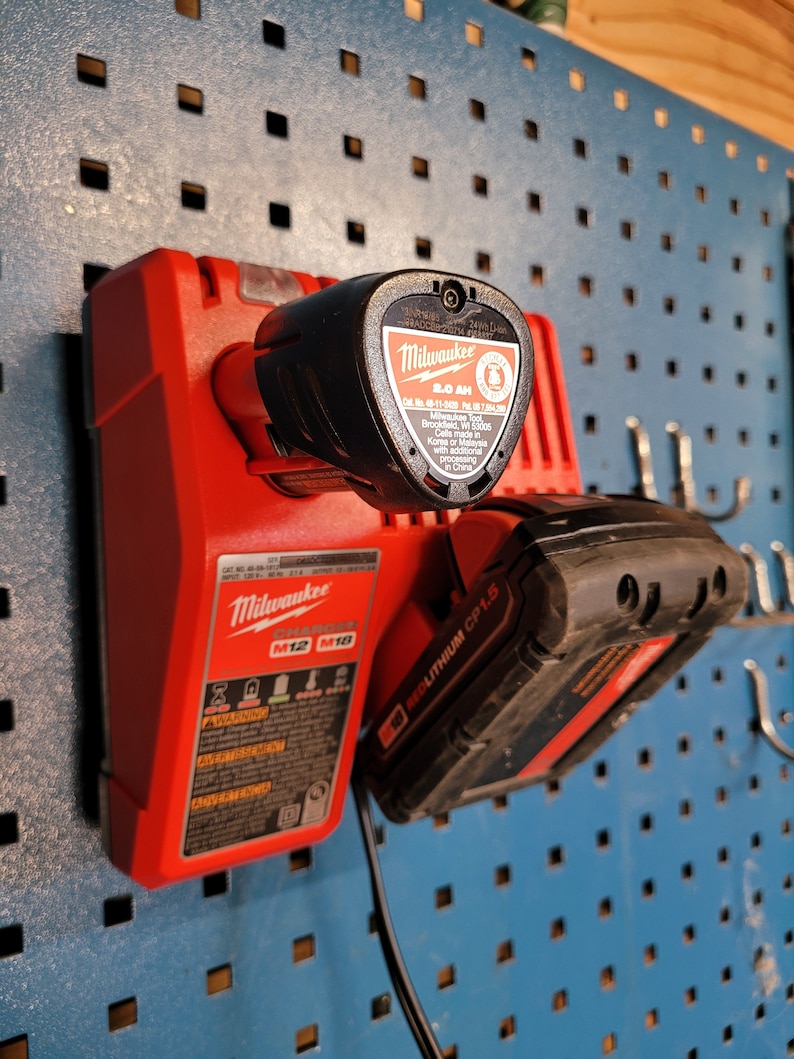 Peut inclure: Un chargeur de batterie d'outil &eacute;lectrique Milwaukee rouge avec une batterie d'outil &eacute;lectrique noire attach&eacute;e. Le chargeur porte l'inscription "Milwaukee M12 M18" et "REDLITHIUM CP1.5". La batterie porte l'inscription "Milwaukee 2.0 AH".