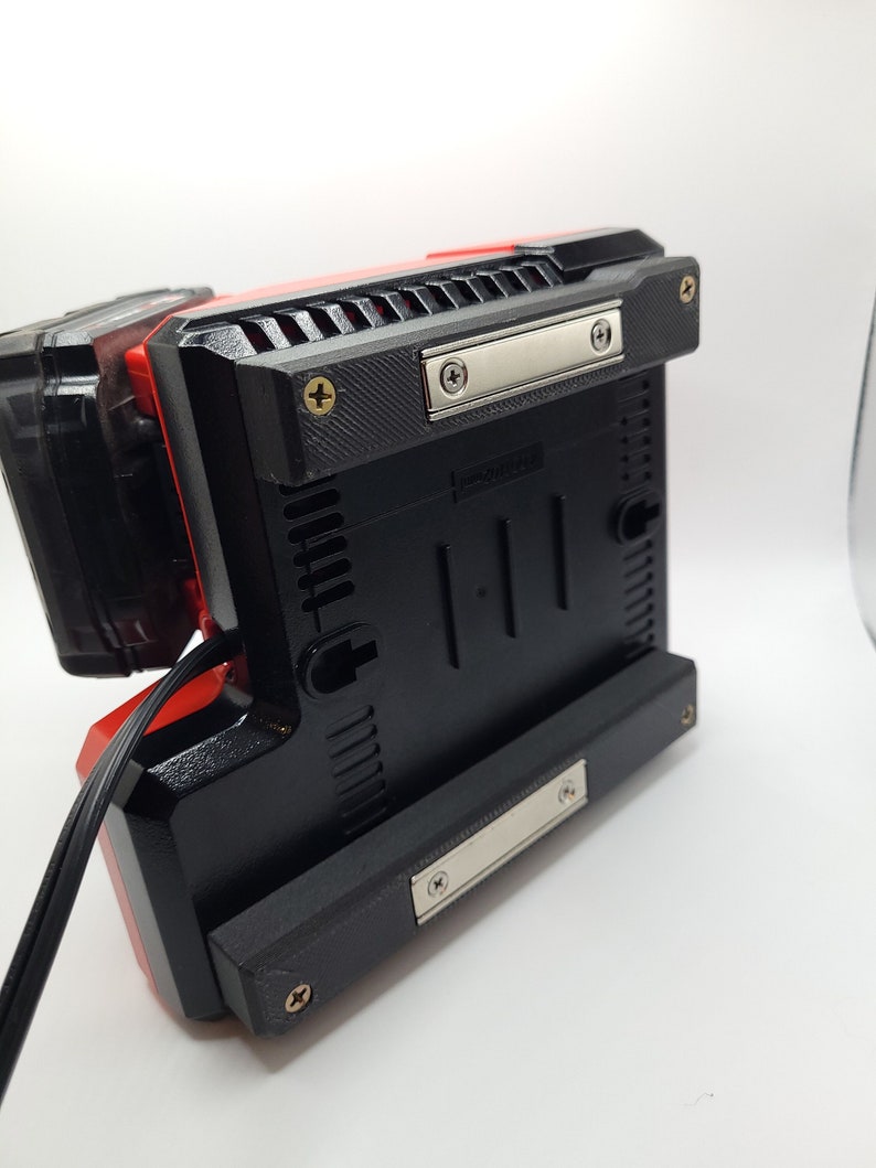 Peut inclure: Un outil &eacute;lectrique noir et rouge avec un cordon noir et une plaque m&eacute;tallique argent&eacute;e sur le dessous. L'outil a une base en plastique noir avec une surface textur&eacute;e et plusieurs vis.