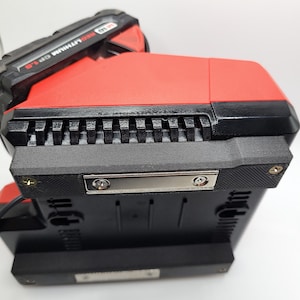 Peut inclure: Un outil &eacute;lectrique rouge et noir avec le texte "18V RED LITHIUM CP 1.5" sur le c&ocirc;t&eacute;. L'outil a une base noire avec une plaque m&eacute;tallique et deux vis.