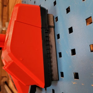 Peut inclure: Une batterie d'outil &eacute;lectrique rouge et noire est mont&eacute;e sur un mur en panneau perfor&eacute; bleu.
