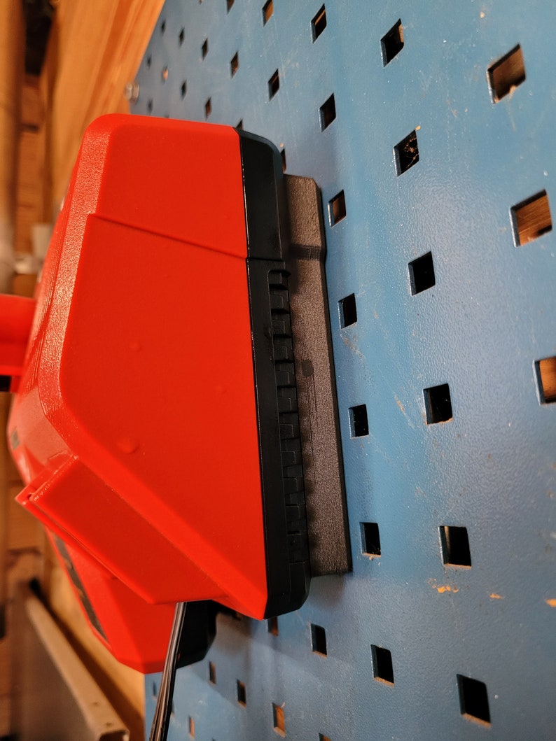 Peut inclure: Une batterie d'outil &eacute;lectrique rouge et noire est mont&eacute;e sur un mur en panneau perfor&eacute; bleu.