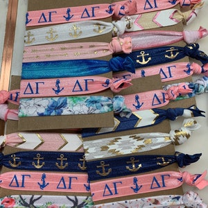 May include: A set of colorful hair ties with a variety of patterns, including anchors, arrows, and floral designs. The hair ties are labeled with the Greek letters "ΔΓ".