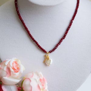 Puede incluir: Un collar de cuentas rojas con un colgante dorado con un diseño de perla y libélula.