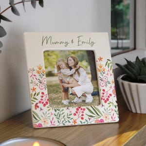 May include: Cream-coloured picture frame with floral accents and the text "Mummy & Emily." The frame holds a photograph of a mother and child. The frame is decorated with colourful flowers and green leaves.