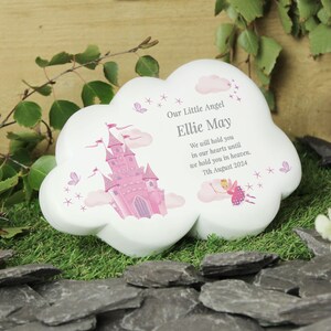 May include: White ceramic cloud-shaped memorial with a pink castle and a fairy illustration. The text reads "Our Little Angel Ellie May We will hold you in our hearts until we hold you in heaven. 7th August 2024."