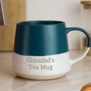 May include: A two-tone ceramic mug with a teal top and a speckled white bottom. The mug has a curved handle and the words "Grandad's Tea Mug" are printed on the front. A perfect gift for tea lovers.