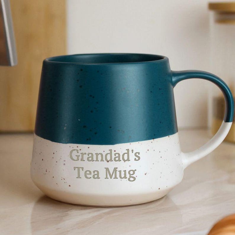 May include: A two-tone ceramic mug with a teal top and a speckled white bottom. The mug has a curved handle and the words "Grandad's Tea Mug" are printed on the front. A perfect gift for tea lovers.