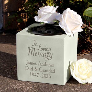 May include: A light green memorial vase with the inscription "In Loving Memory" and the name "James Andrews Dad & Grandad 1947-2026". The vase is filled with white roses.
