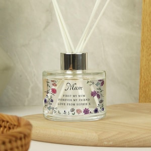 May include: A glass diffuser bottle with a silver cap and white reeds. The bottle is decorated with floral designs in pink, purple, and blue, and features the word "Mum" and a personalized message.