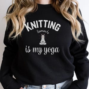 Op de afbeelding: Zwarte sweatshirt met de witte tekst "Knitting llamaste is my yoga". Een witte lama in yogahouding is gecentreerd onder het woord "llamaste". De sweatshirt heeft lange mouwen en een ronde hals.