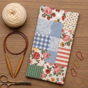 May include: A patchwork fabric case with floral and gingham patterns, a ball of yarn, knitting needles, scissors, and stitch markers on a wooden surface. The case has a white button closure. The yarn is cream-coloured.