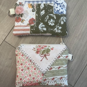 May include: Two small, patchwork fabric coin purses with zip closures. One features floral patterns in pink, red, and white, the other has a green and white floral design. Each has a small loop for attaching to a keyring.