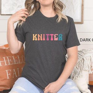 Puede incluir: Una camiseta gris oscuro con la palabra "KNITTER" impresa en colores arco&iacute;ris en la parte delantera.