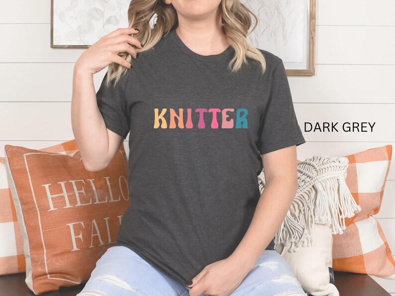 Puede incluir: Una camiseta gris oscuro con la palabra "KNITTER" impresa en colores arco&iacute;ris en la parte delantera.