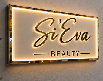 May include: A rectangular wall-mounted sign with a gold metallic frame and a white face. The sign features the text Si'Eva in a gold cursive script and the word BEAUTY in gold block letters, both illuminated by a warm internal LED glow.