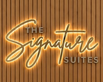 May include: A wall-mounted sign featuring the text THE SIGNATURE SUITES in a combination of block and script lettering. The word Signature is illuminated with a warm golden glow, set against a vertical brown wood slat paneling background.