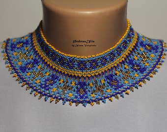 May include: A beaded choker necklace with a geometric pattern in blue, yellow, and gold. The necklace is made of small beads and has a fringe at the bottom. The text "PrekrasZilia by Ziliana Vasylenka" is printed on the necklace.