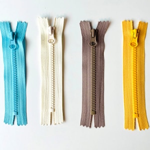 May include: Four different zipper pulls in various colors, including blue, white, brown, and yellow. The zippers are all closed and have a metal slider.