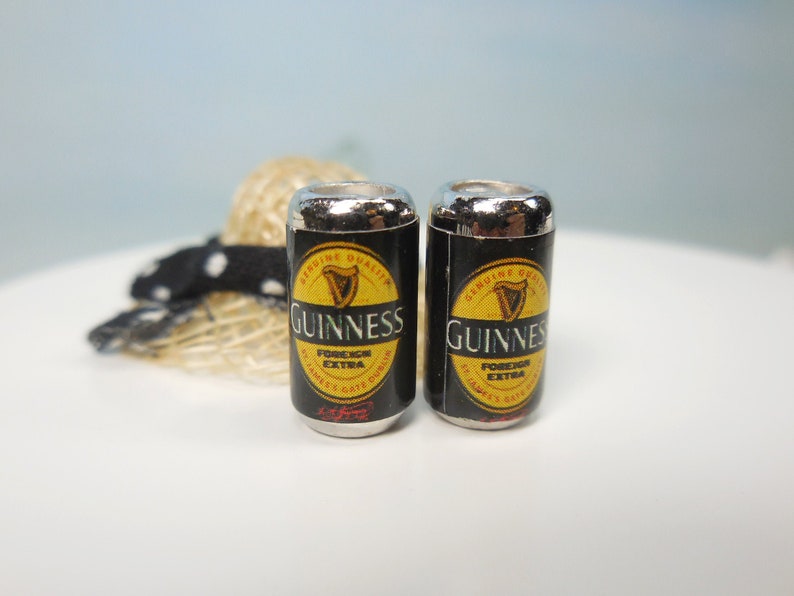 May include: Two silver-topped cans of Guinness Foreign Extra Stout beer. The cans are black with a yellow label featuring the Guinness harp logo and the text "Guinness Foreign Extra Stout".