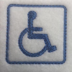 May include: Two embroidered patches featuring the international symbol of access. Each patch has a blue wheelchair user icon within a white square, framed by a blue border. The patches are on a white, textured background.