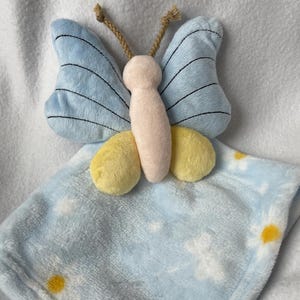 May include: A light blue baby blanket with a white daisy pattern and a plush blue and yellow butterfly attached.