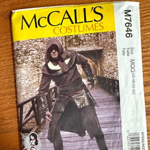 May include: A McCall's Costumes sewing pattern envelope M7646 in size MQQ (46-48-50-52). The front features a photograph of a person wearing a hooded brown tunic with metallic-look armor plates, a wide belt, and dark trousers. The text includes the brand name.