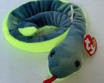 Pode incluir: Brinquedo de cobra de pelúcia verde e amarelo com língua vermelha. A cobra está enrolada em um círculo e tem uma etiqueta Ty.