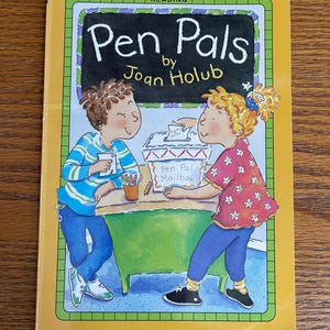 May include: A yellow book cover with a green chalkboard that says "Pen Pals" by Joan Holub. There are two children, one with brown hair and one with blonde hair, standing in front of a green table with a red and white mailbox that says "Pen Pal Mailbox".