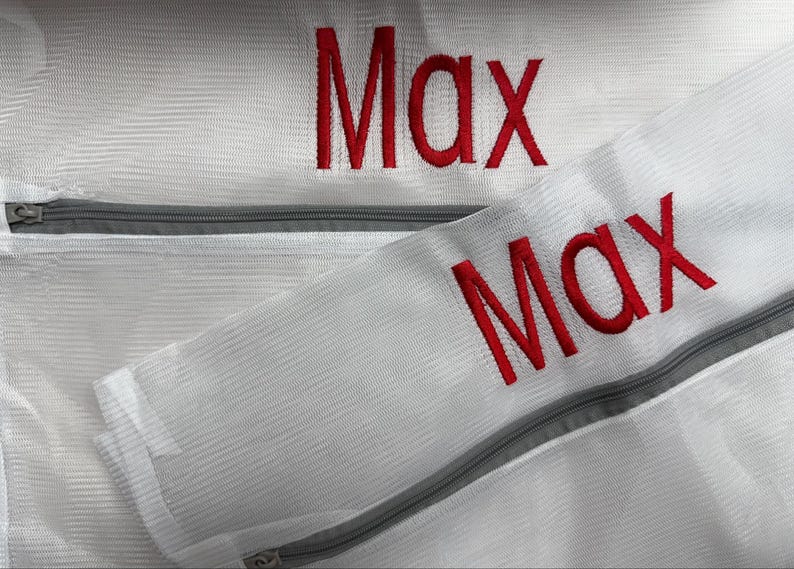 K&ouml;nnte beinhalten: Nahaufnahme von zwei wei&szlig;en W&auml;schebeuteln aus Mesh mit grauen Rei&szlig;verschl&uuml;ssen. Der Name "Max" ist rot auf beiden Beuteln gestickt. Die Beutel sind f&uuml;r die W&auml;sche empfindlicher Artikel gedacht.