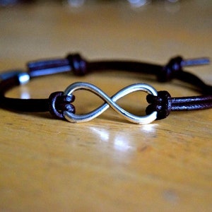 May include: A brown leather bracelet with a silver infinity symbol charm.