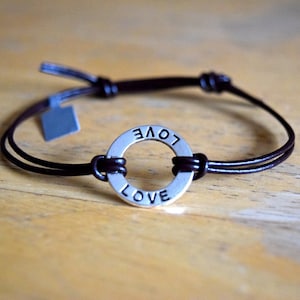 May include: A brown leather bracelet with a silver charm that says "LOVE" on it.