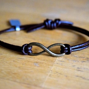 May include: A brown leather bracelet with an infinity symbol charm. The charm is made of metal and has a dark bronze finish.