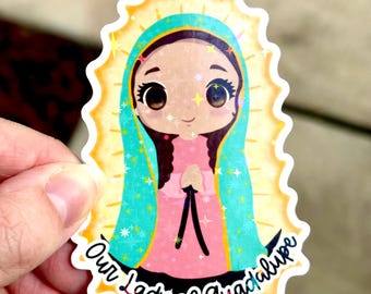 May include: A sticker featuring a cartoon illustration of Our Lady of Guadalupe. The image shows a woman in a pink dress and teal shawl, surrounded by a golden halo. The text "Our Lady of Guadalupe" is written in black script.